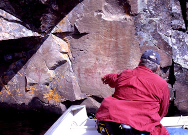 A researcher points out a rock art panel on Mazinaw Rock. The paintings can only be approached by boat — except in winter if ice on the lake is thick enough.