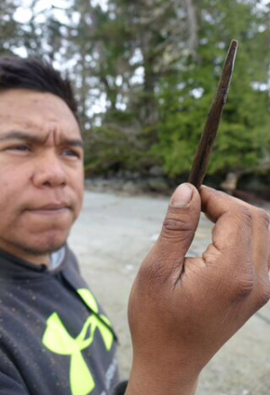 Josh Vickers, of the Heiltsuk First Nation and the archeological team, holds up a rare 6,500 year old carved wooden bi-point. 