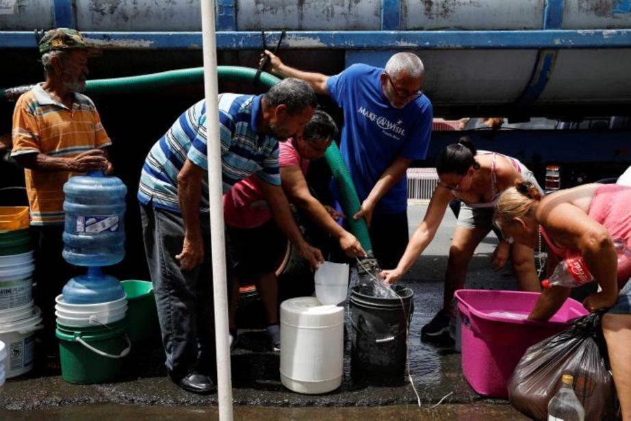 People queue to fill containers with water from a tank truck at an area hit by Hurricane Maria in Canovanas, Puerto Rico, September 26, 2017.