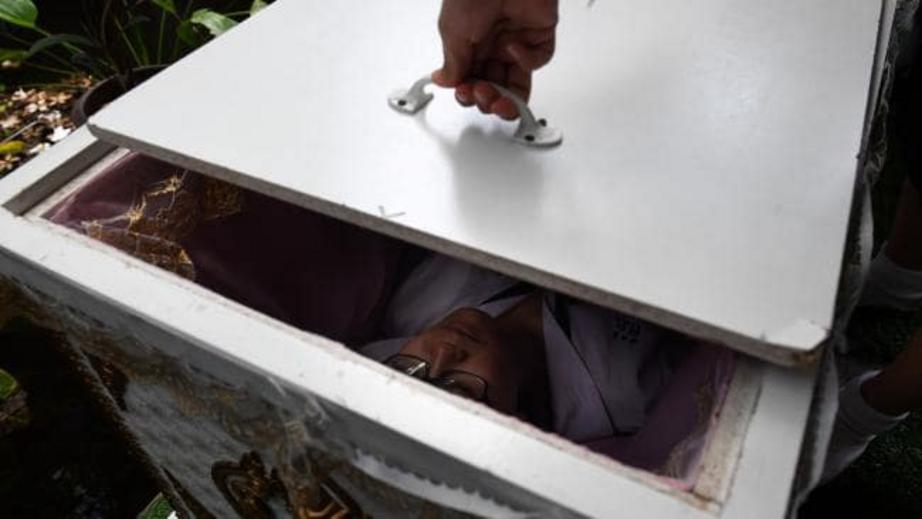 A Thai teenager tries out a traditional coffin at the Kid Mai Death Awareness Cafe in Bangkok, Thailand.